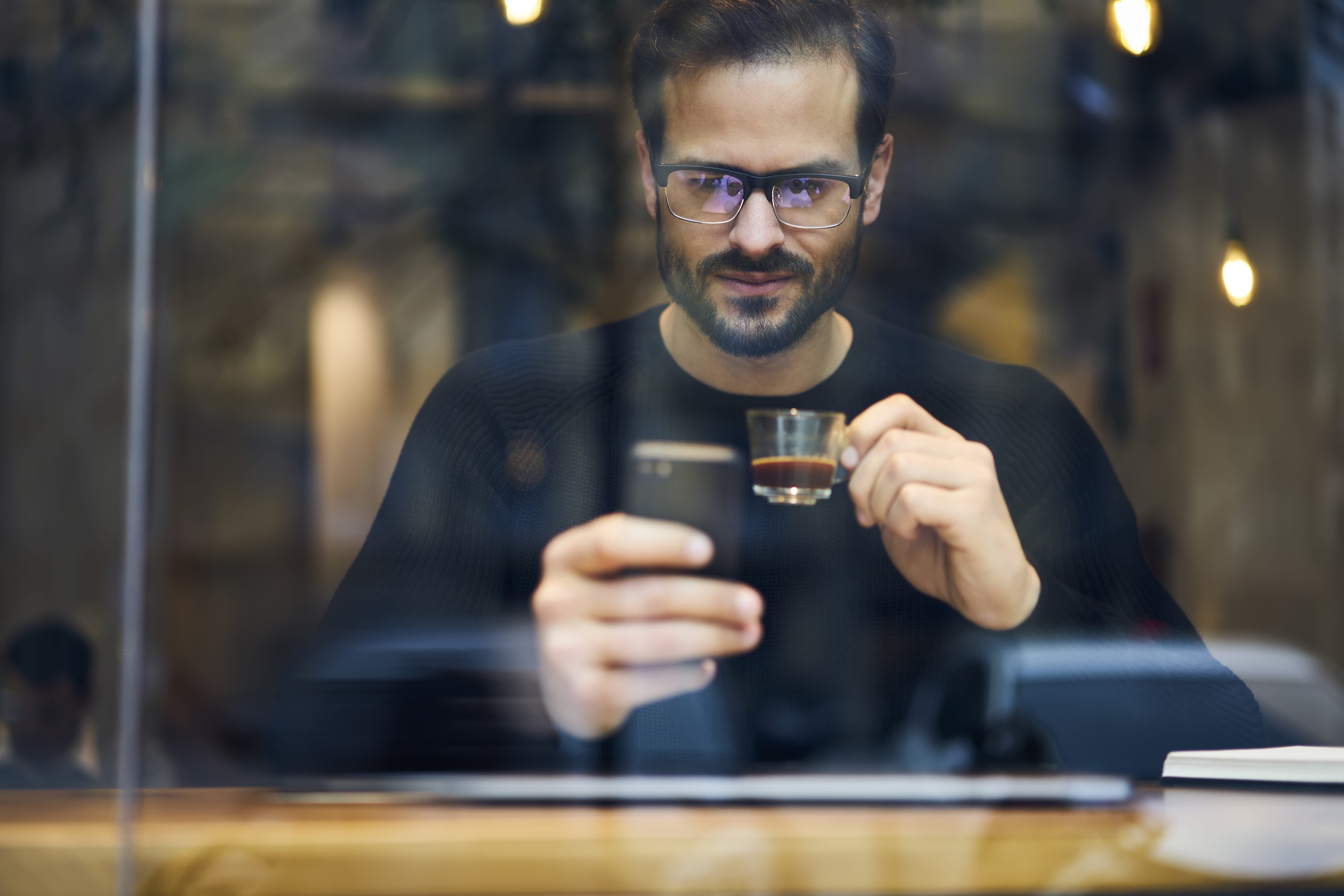 Smiling ethnic man with coffee surfing smartphone